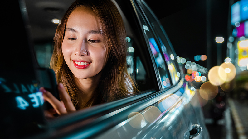 Asian businesswoman commuting from office in Taxi backseat with mobile phone on road in city at night after late work.