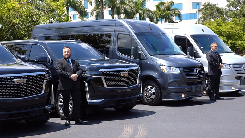 Chauffeurs standing in front of a fleet of luxury transportation vehicles, including Cadillac SUVs and Mercedes vans, in Miami.