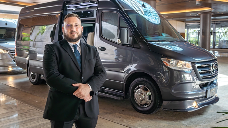 Professional chauffeur standing beside a luxury Mercedes van in Miami.