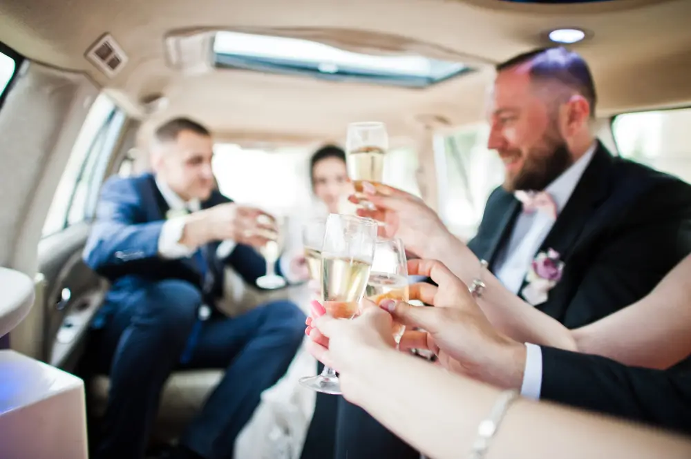 Groomsmen with bridesmaids and wedding couple drinking champagne in the limo.
