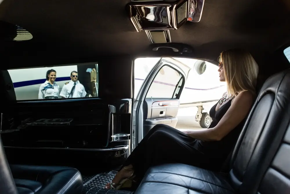 Elegant woman in limousine with airhostess and pilot near private jet at terminal
